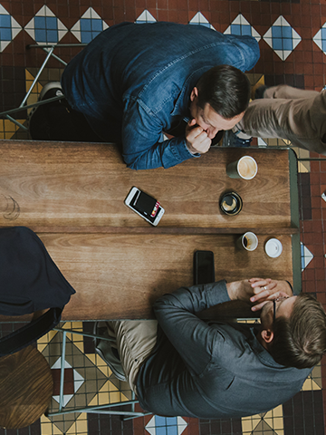 Over head shot of two business men meeting over coffee with a southwest motif tile floor under their wooden table